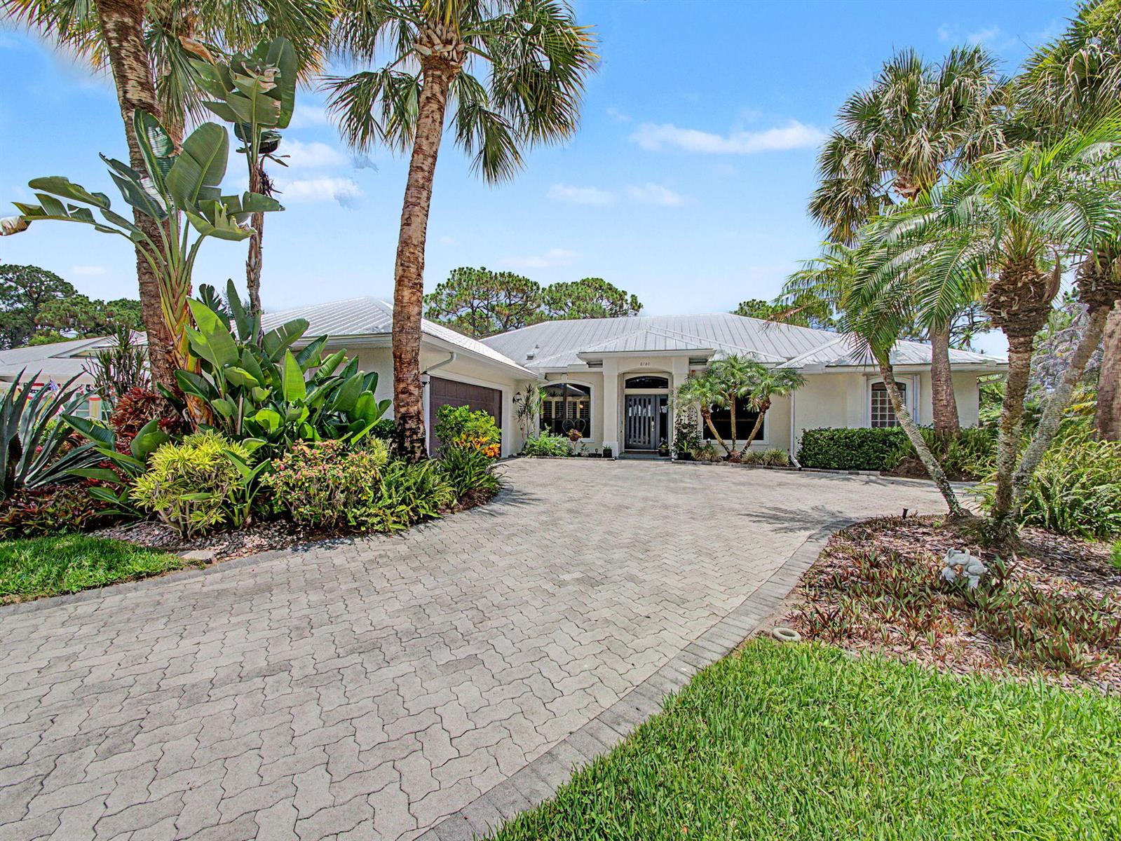 A single-story house with a paved driveway, metal roof, and lush tropical landscaping — 8780 SW Fishermans Wharf Drive, Stuart FL 34997, STUART, FL