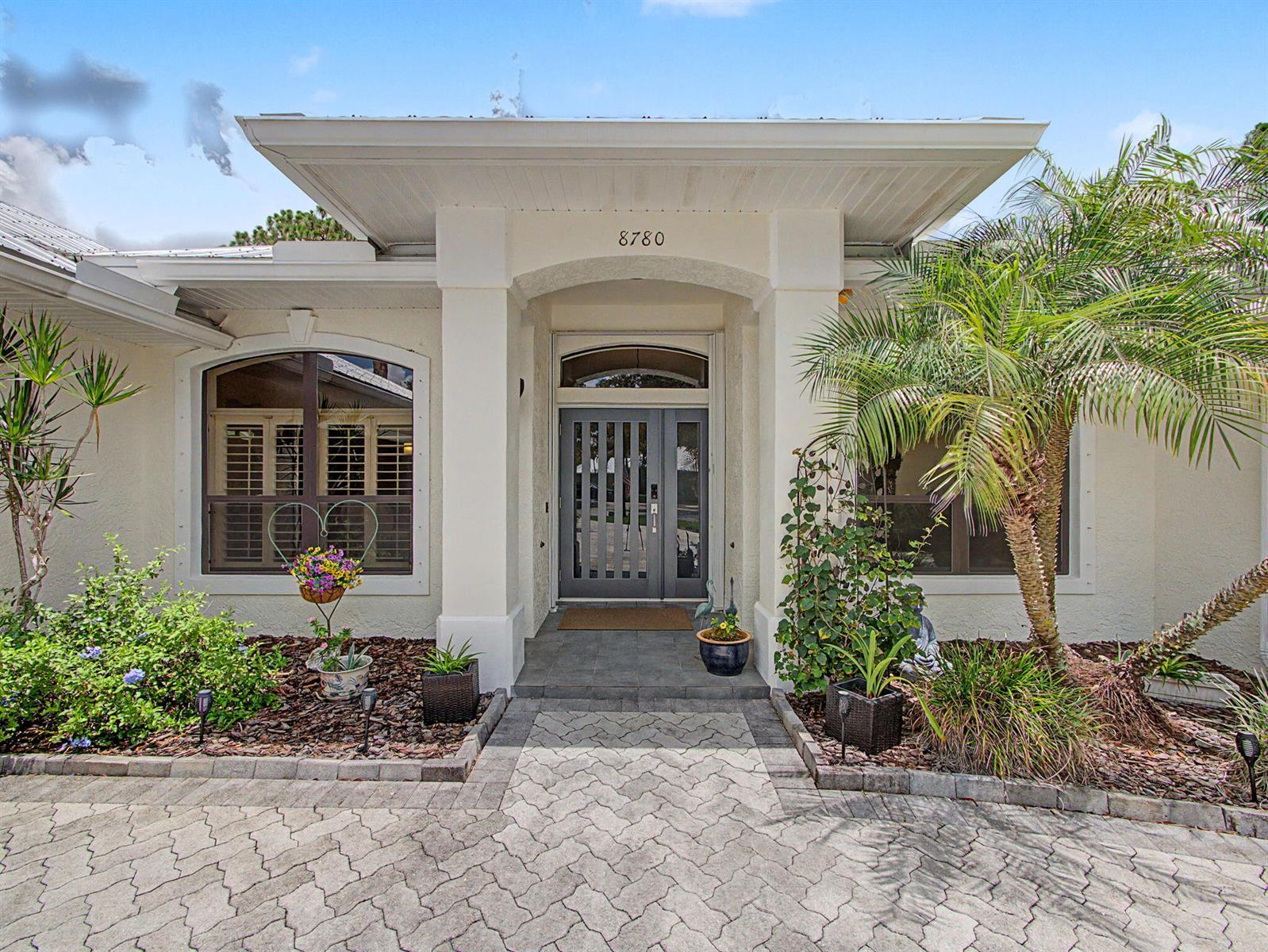 The exterior of a house features a paved walkway leading to a gray double front door — 8780 SW Fishermans Wharf Drive, Stuart FL 34997, STUART, FL