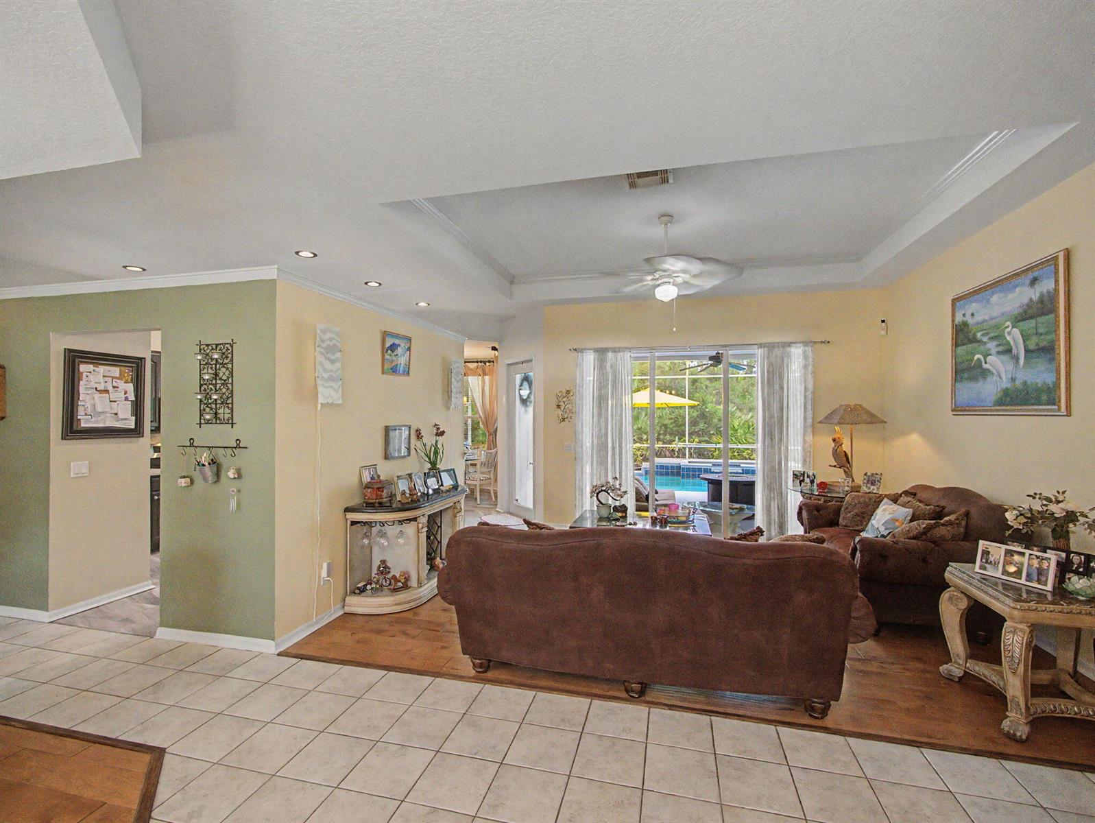 A living room features brown sofas, tile and wood flooring, and a view of a pool — 8780 SW Fishermans Wharf Drive, Stuart FL 34997, STUART, FL