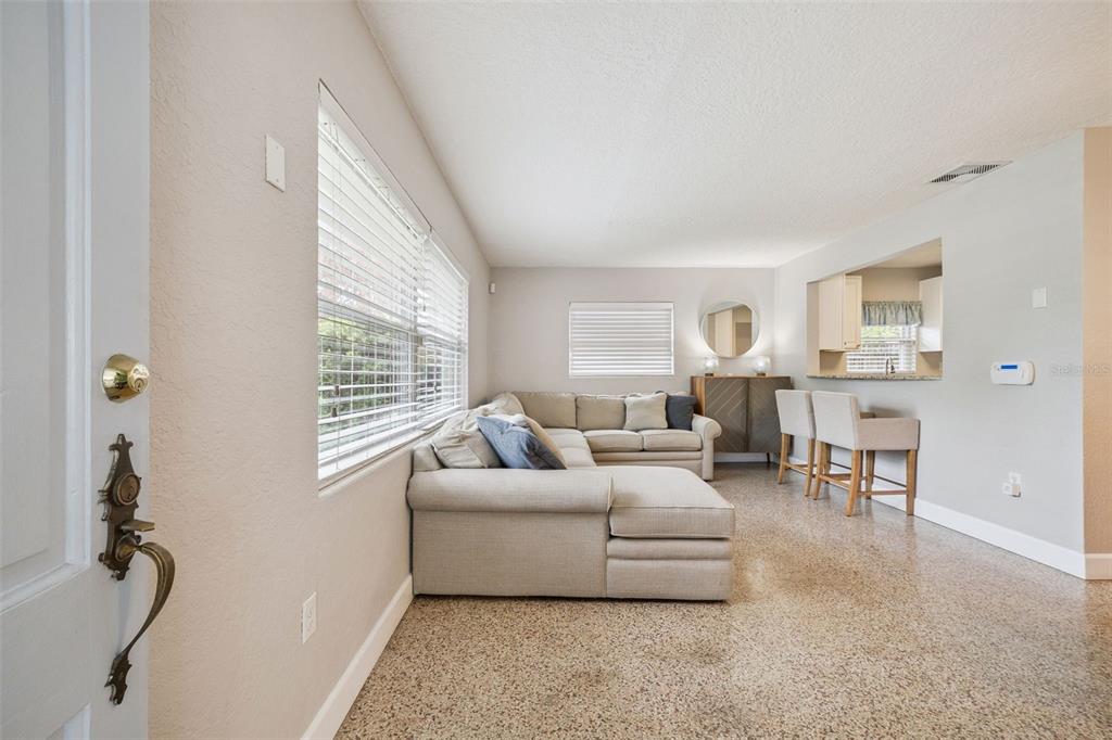 A living room features a beige sectional sofa, large windows, and speckled terrazzo flooring — 2513 MUSSELWHITE AVENUE, ORLANDO, FL