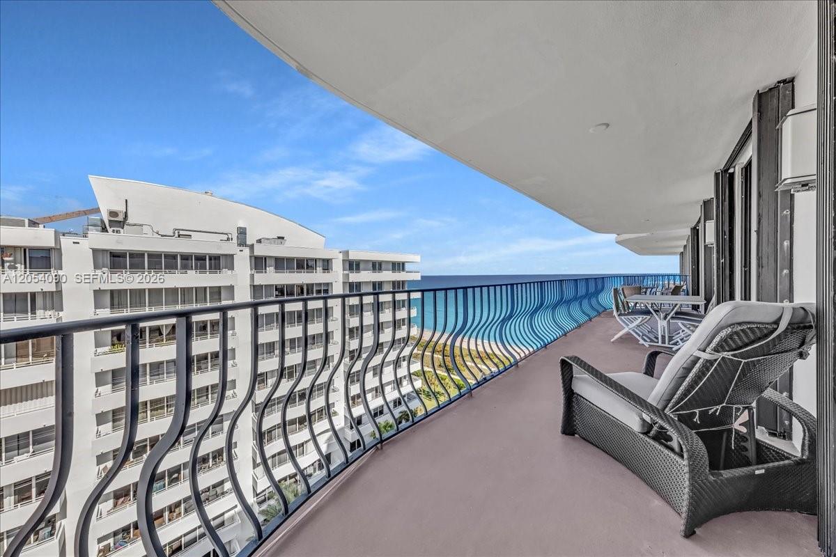 A balcony with a black metal railing overlooks the ocean and a neighboring apartment building — 8877 Collins Ave # 2, Surfside FL 33154, SURFSIDE, FL