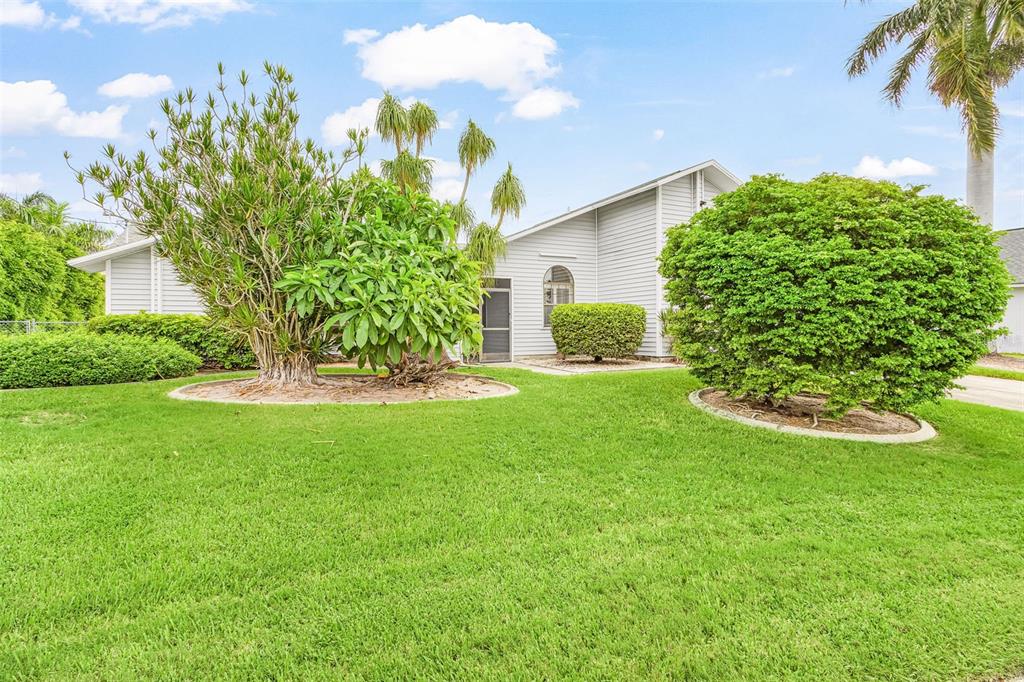 A light-colored house exterior features a large green lawn, mature trees, and manicured shrubs — 4903 SW 11TH PLACE, CAPE CORAL, FL