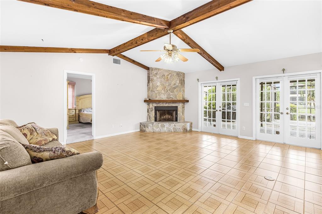A living room features vaulted ceilings with exposed wood beams, tile flooring, and a stone fireplace — 4903 SW 11TH PLACE, CAPE CORAL, FL