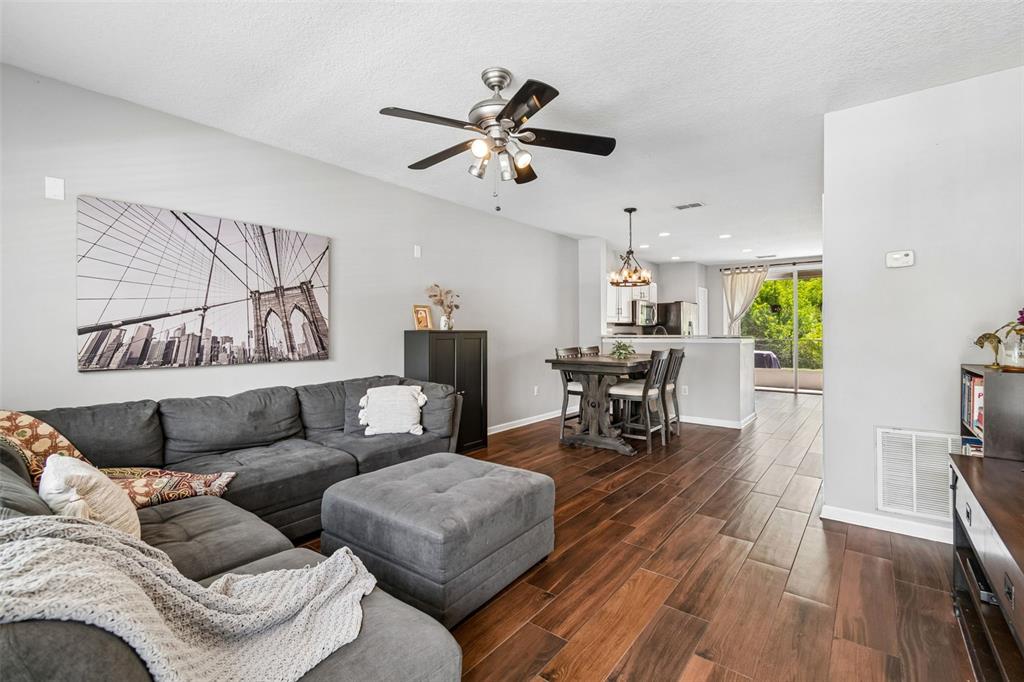 A living room with wood-look tile floors, a gray sectional sofa, and an adjacent dining area — 4423 BARNSTEAD DR, RIVERVIEW, FL