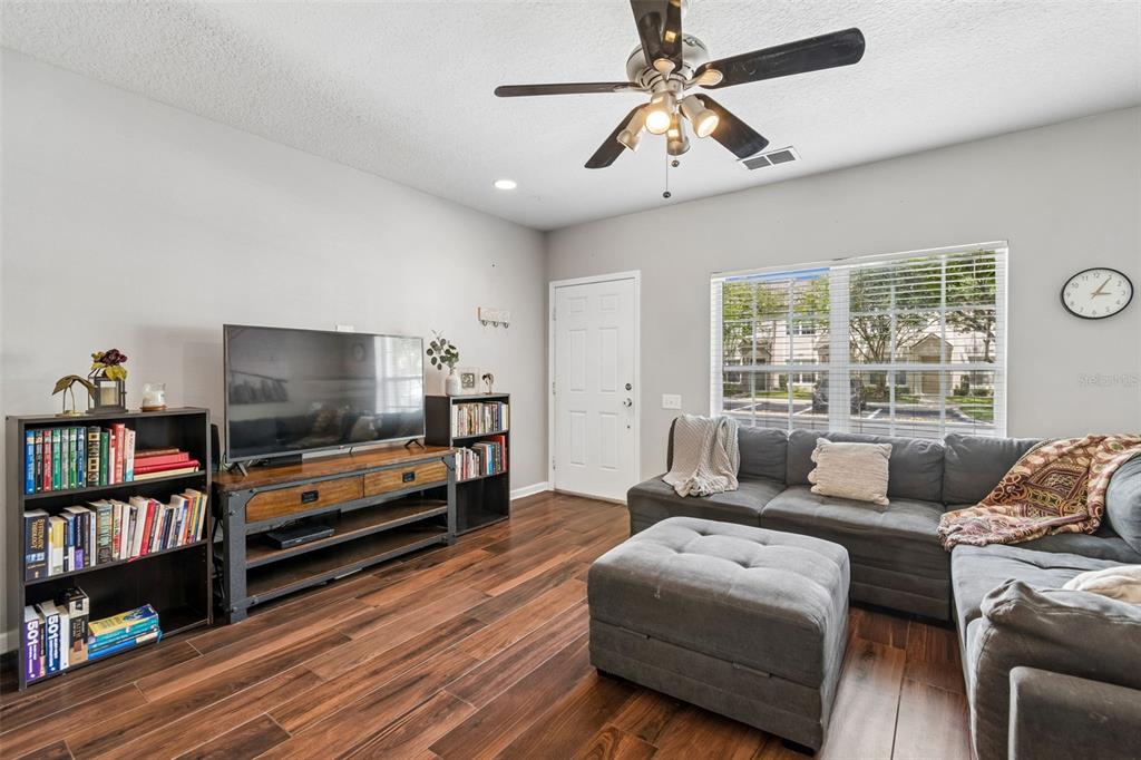 A living room features wood-look flooring, a gray sectional sofa, a television console, and bookshelves — 4423 BARNSTEAD DR, RIVERVIEW, FL