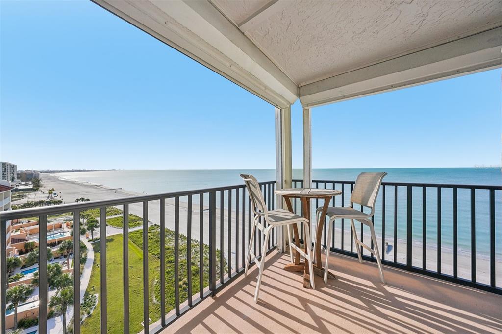 A balcony with a table and two chairs overlooks a sandy beach and ocean — 15316 GULF BOULEVARD UNIT 801, MADEIRA BEACH, FL
