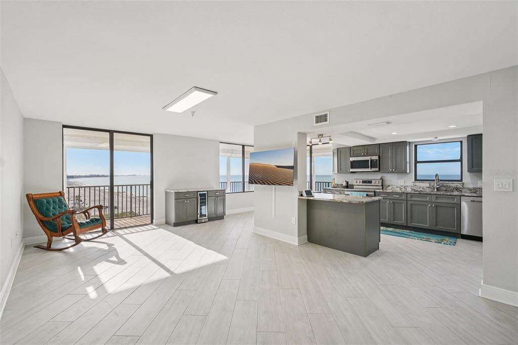 A bright living area with light wood-look floors, a kitchen, and a balcony overlooking water — 15316 GULF BOULEVARD UNIT 801, MADEIRA BEACH, FL