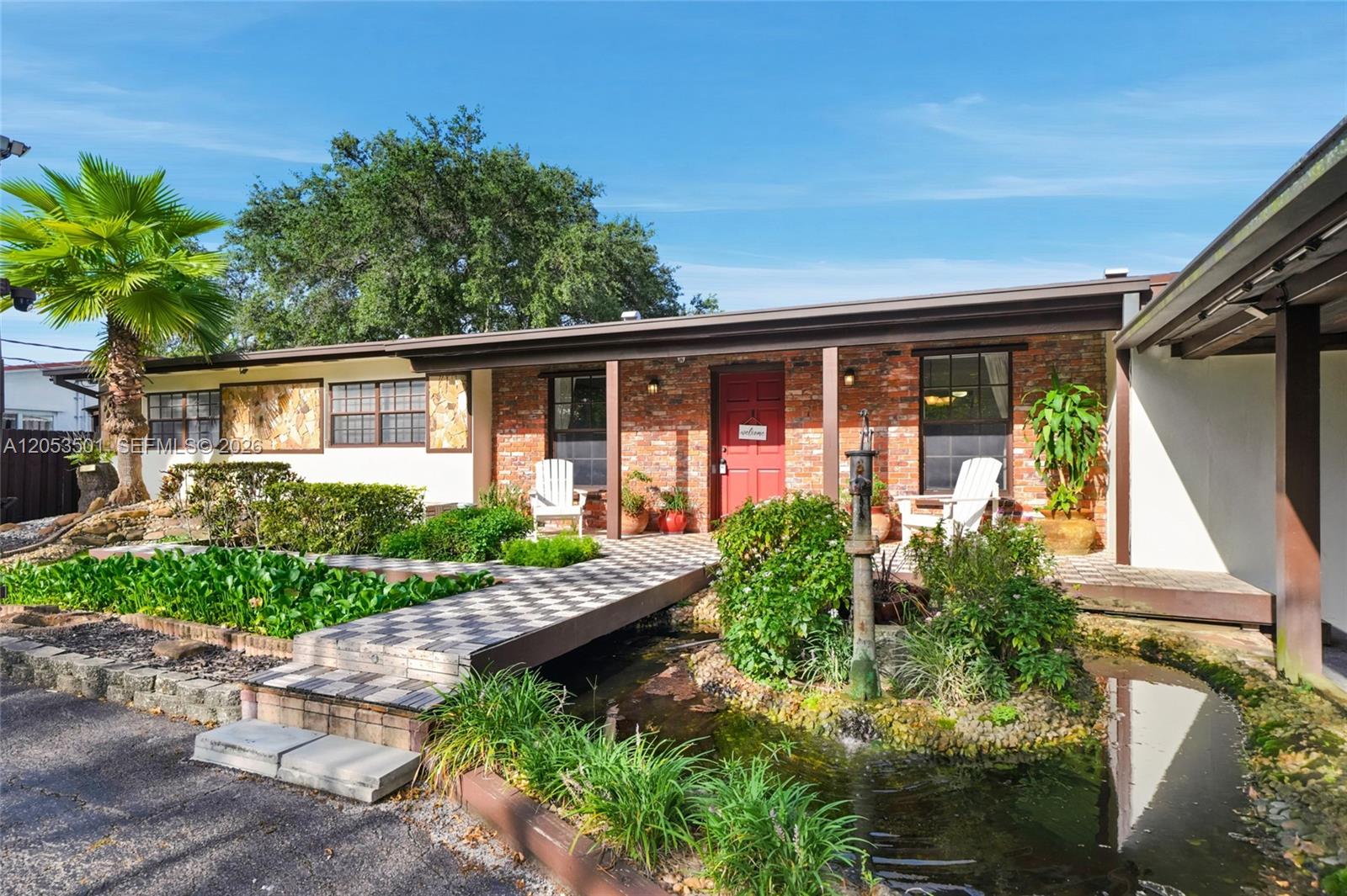 A brick house features a checkerboard walkway over a pond with a water pump — 15425 N Miami Ave, Miami FL 33169, MIAMI, FL