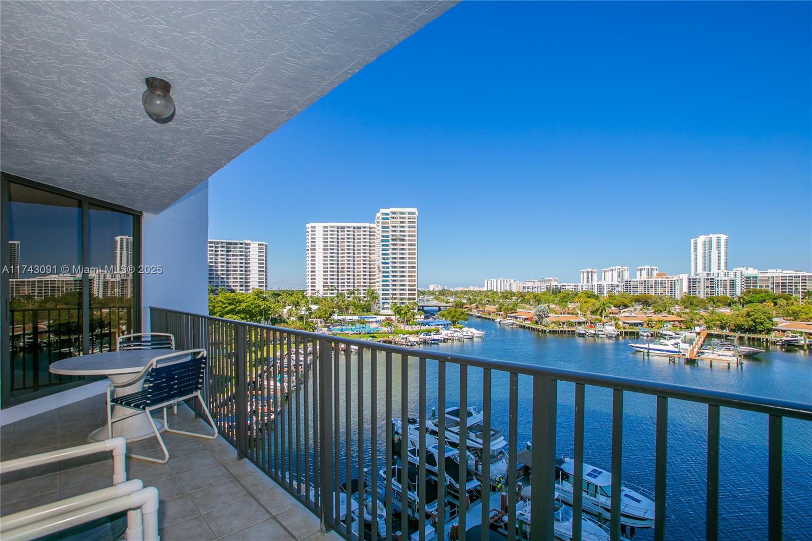 A balcony with outdoor furniture overlooks a waterway filled with boats and high-rise buildings — 300 Three Islands Blvd # 406, Hallandale Beach FL 33009, HALLANDALE BEACH, FL