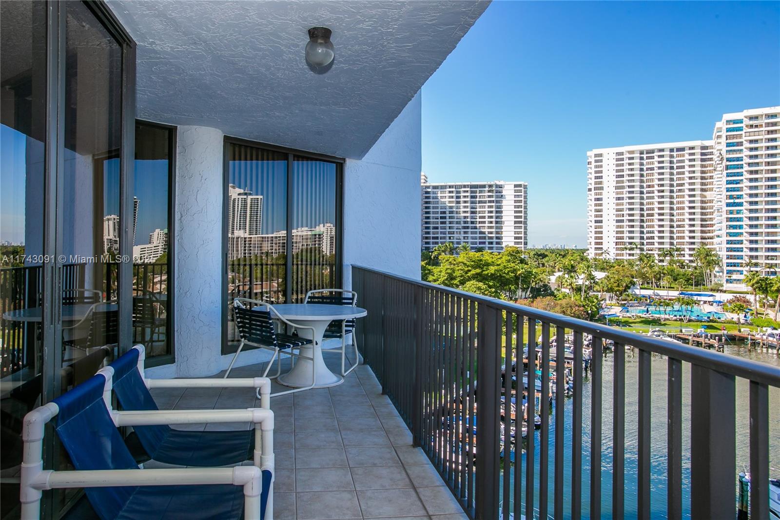 A balcony with patio furniture overlooks a canal and high-rise buildings under a clear sky — 300 Three Islands Blvd # 406, Hallandale Beach FL 33009, HALLANDALE BEACH, FL