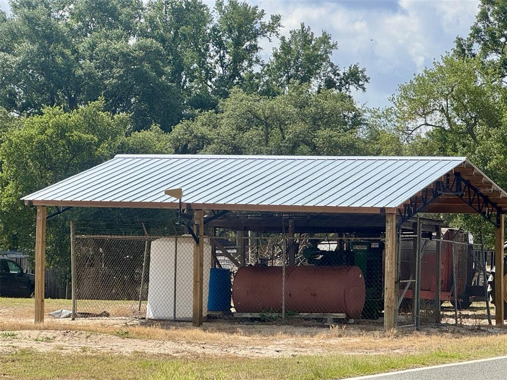 A metal-roofed open-sided shed stands in a grassy area enclosed by chain-link fencing — CROOKED LAKE DRIVE N, BABSON PARK, FL