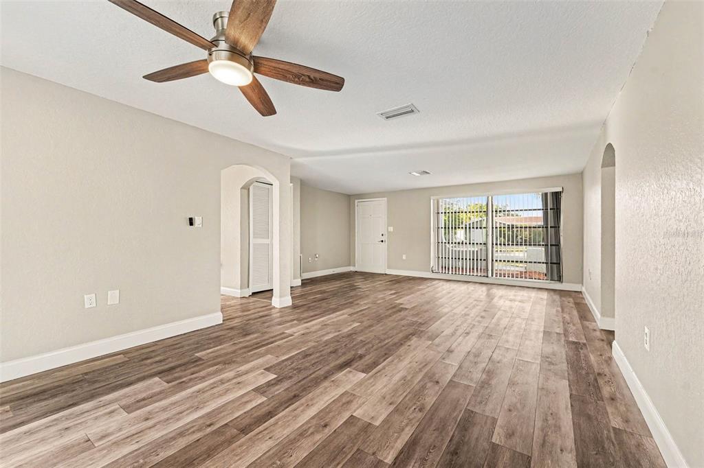 An empty living room features wood-look flooring, a ceiling fan, and sliding glass patio doors — 3207 SALISBURY DRIVE, HOLIDAY, FL