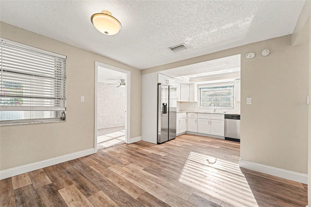 A dining area with wood-look flooring opens into a white kitchen with stainless steel appliances — 3207 SALISBURY DRIVE, HOLIDAY, FL