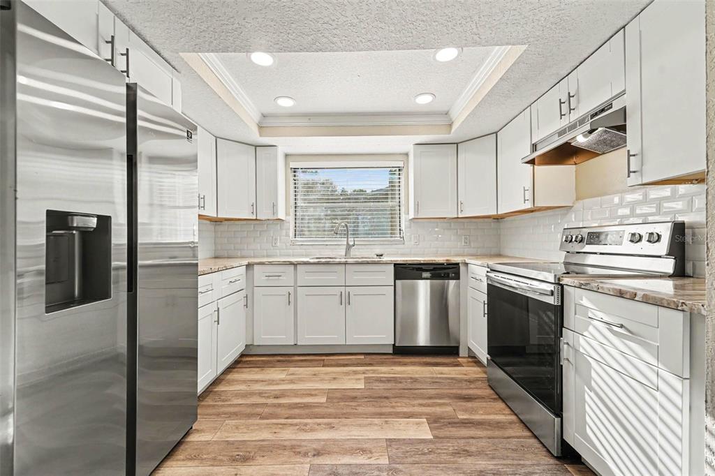 A kitchen features white cabinets, stainless steel appliances, subway tile backsplash, and wood-look flooring — 3207 SALISBURY DRIVE, HOLIDAY, FL
