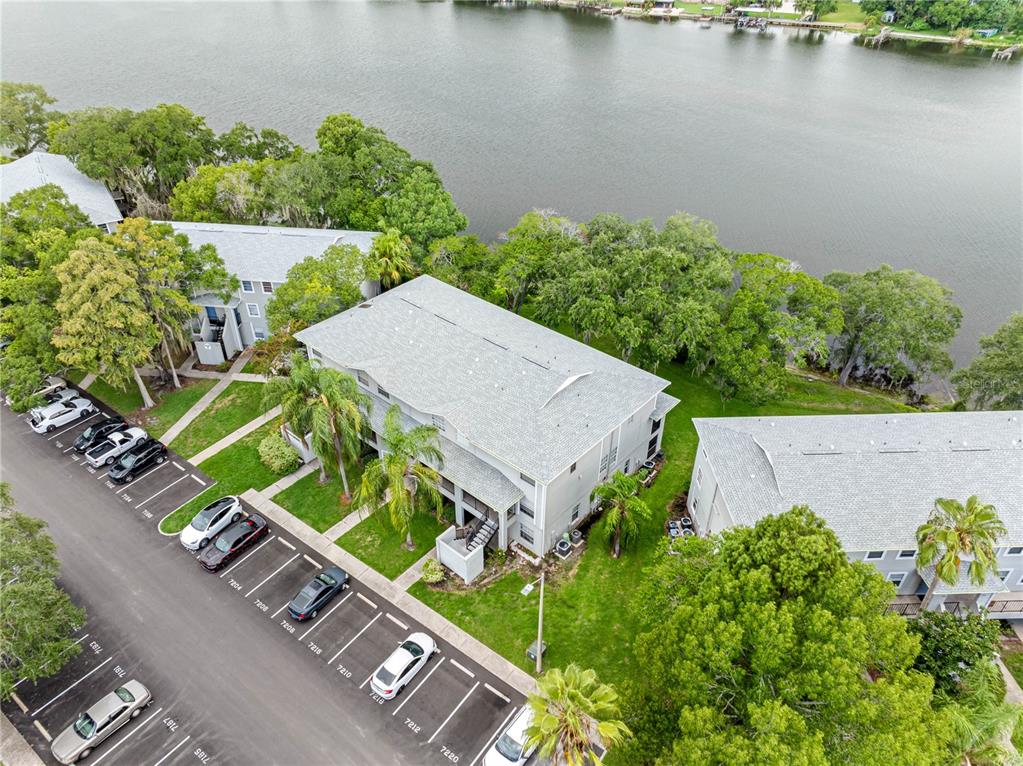 An aerial view shows apartment buildings with parking spaces and a lake in the background — 7200 E BANK DRIVE UNIT 0, TAMPA, FL