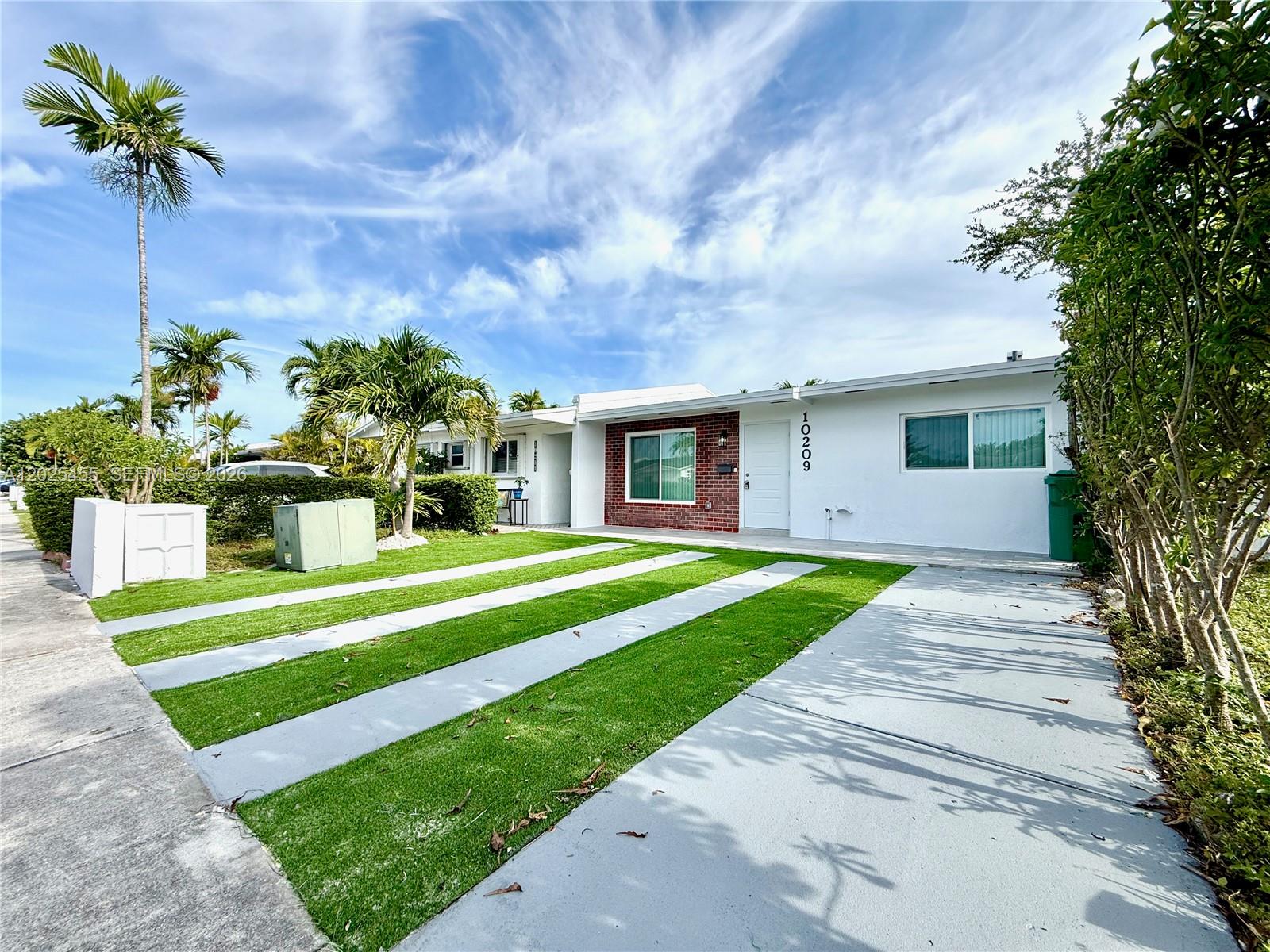 A single-story house features a white facade, a brick accent wall, and a striped driveway — 10209 SW 20th Ter, Miami FL 33165, MIAMI, FL