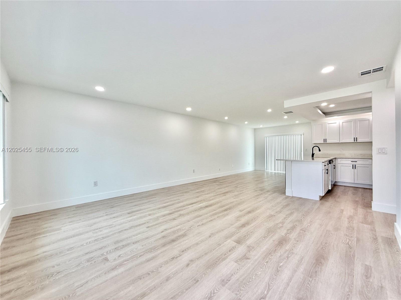An open-concept living area features light wood-look flooring, recessed lighting, and a white kitchen — 10209 SW 20th Ter, Miami FL 33165, MIAMI, FL