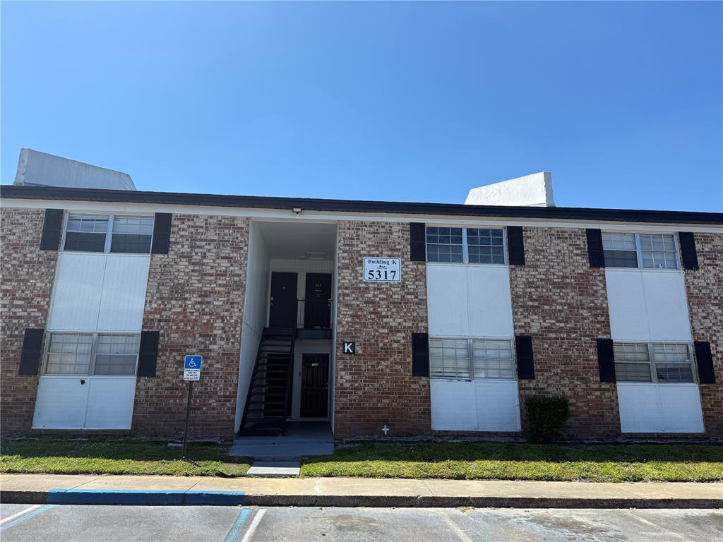 A two-story brick apartment building features a central stairwell and a handicap parking sign — 5317 CURRY FORD ROAD UNIT 103, ORLANDO, FL