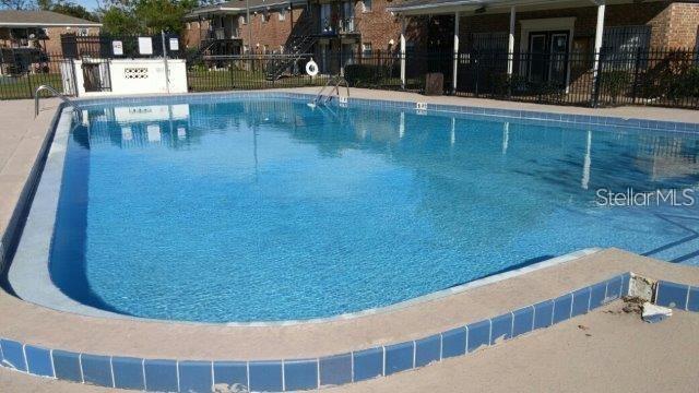 An outdoor swimming pool with a blue tiled edge sits in front of apartment buildings — 5317 CURRY FORD ROAD UNIT 103, ORLANDO, FL