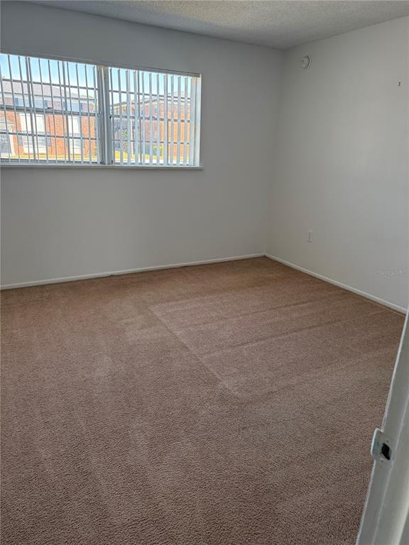 An empty bedroom features beige carpeting, white walls, and a window with vertical blinds — 5317 CURRY FORD ROAD UNIT 103, ORLANDO, FL