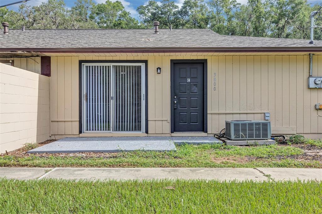Exterior view of a single-story unit with a black door, sliding glass door, and AC unit — 3800 SE 17TH CT UNIT C, OCALA, FL