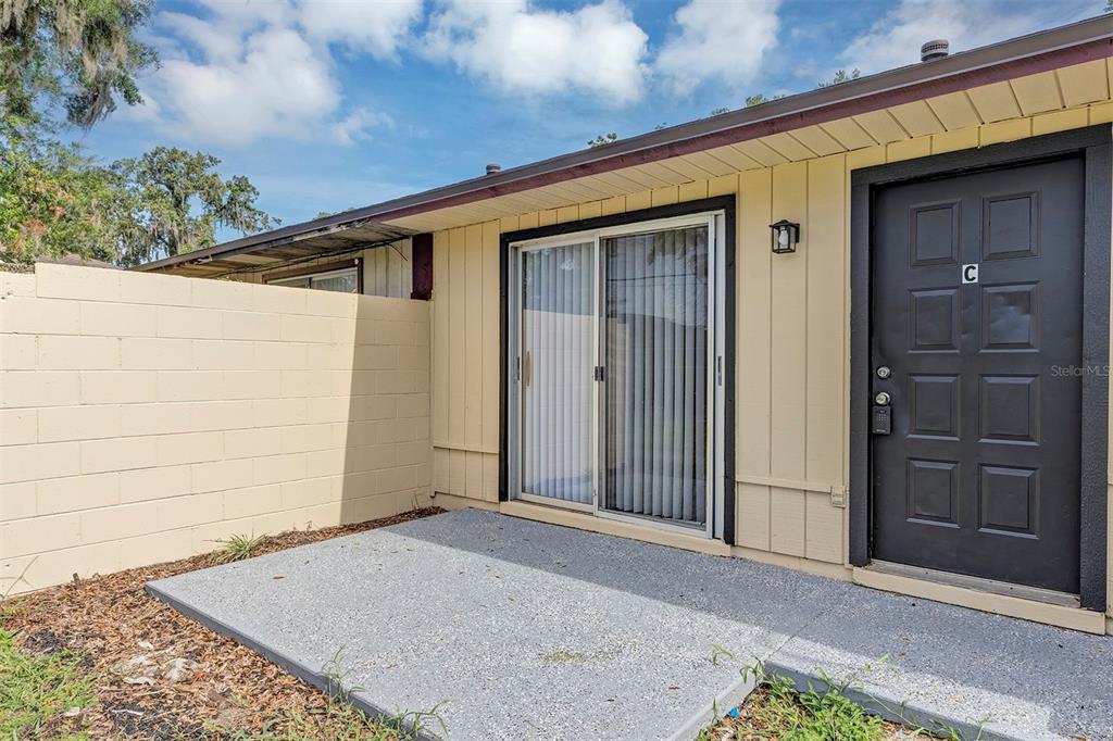 A concrete patio sits outside a sliding glass door and a dark door labeled C — 3800 SE 17TH CT UNIT C, OCALA, FL