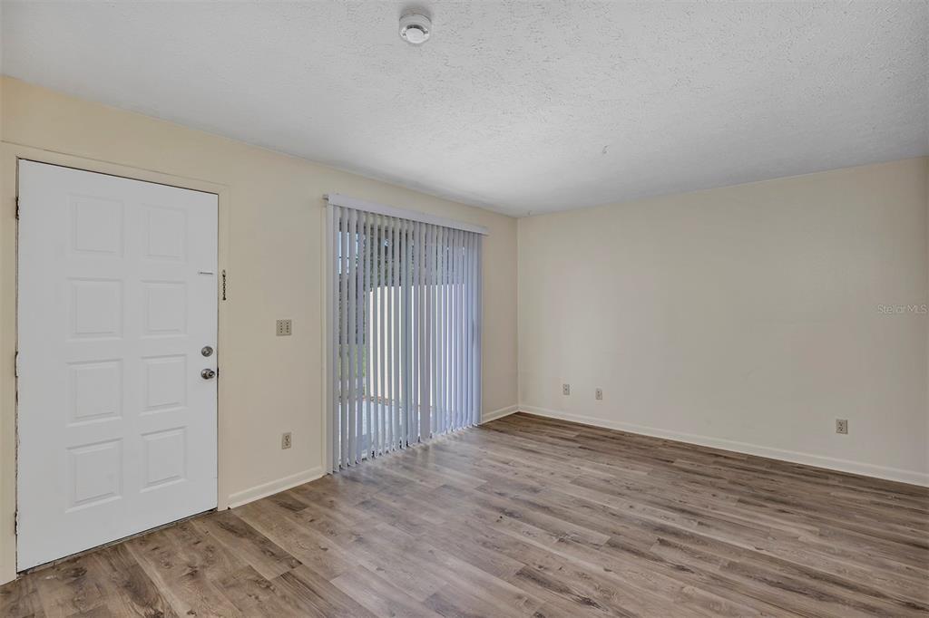 An empty room features light-colored walls, wood-look flooring, a white entry door, and sliding doors — 3800 SE 17TH CT UNIT C, OCALA, FL