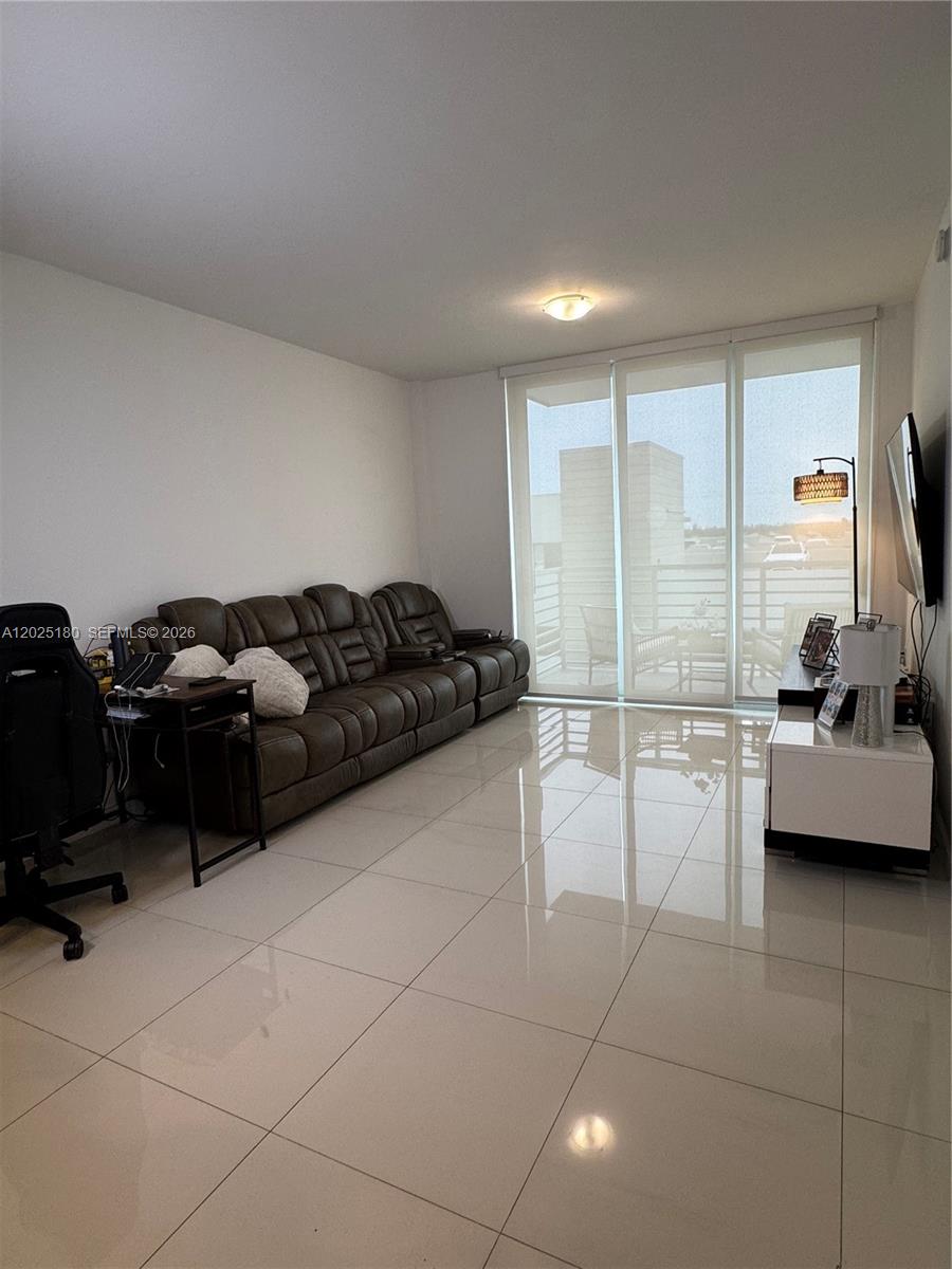 A living room features a brown leather sofa, white tile floors, and a glass balcony door — 7875 NW 107th Ave # 602, Doral FL 33178, DORAL, FL