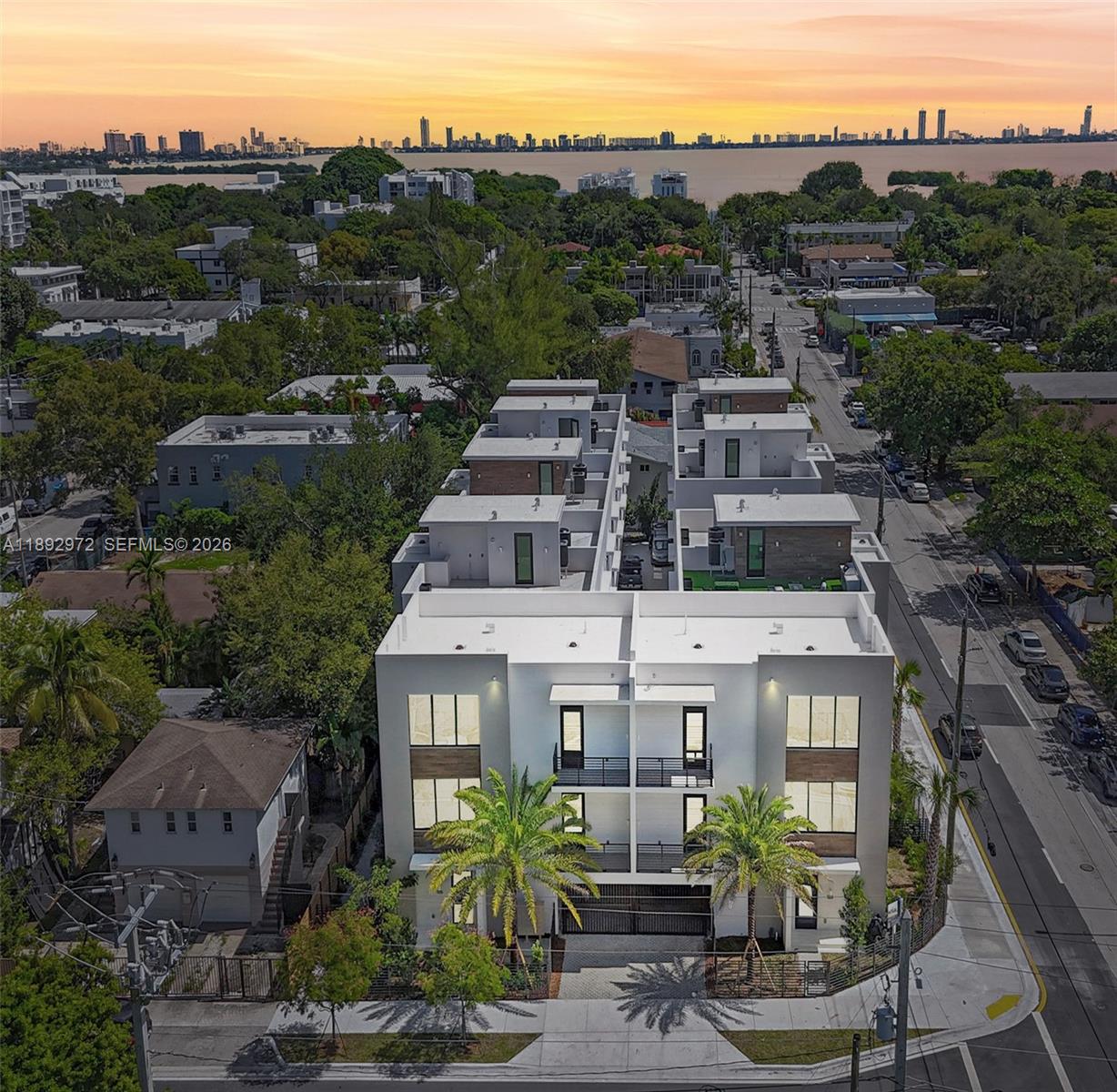 An aerial view shows a modern white apartment building surrounded by trees near a bay — 503 NE 61st St, Miami FL 33137, MIAMI, FL