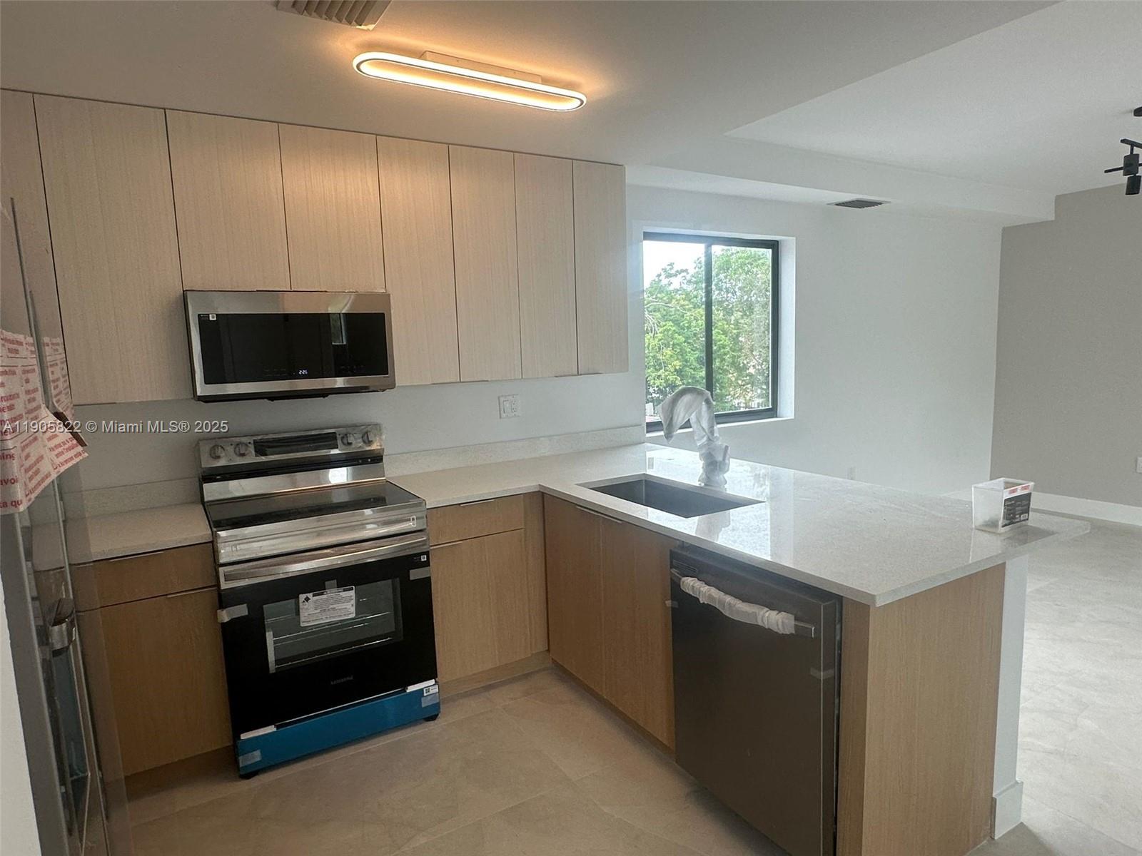 A modern kitchen features light wood cabinets, stainless steel appliances, and a white quartz countertop — 5423 NE Miami Ct # 7, Miami FL 33137, MIAMI, FL