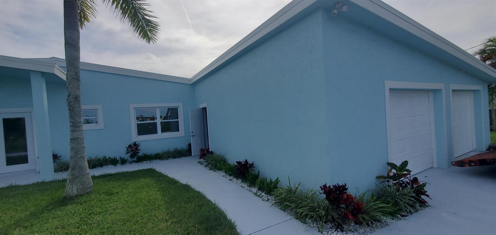 A light blue house exterior features a white walkway, two garage doors, and landscaping — 1529 Thumb Point Drive, Fort Pierce FL 34949, FORT PIERCE, FL