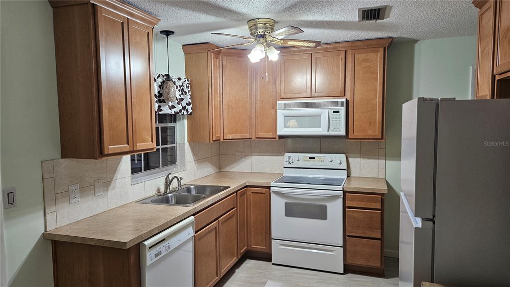 A kitchen features wood cabinets, white appliances, a double sink, and a tiled backsplash — 662 N CHARLES AVENUE, INVERNESS, FL