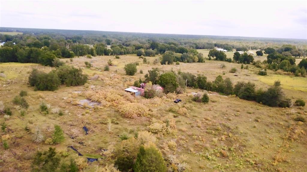 An aerial view shows a small, weathered house surrounded by overgrown fields and scattered trees — 14385 SW HIGHWAY 484, DUNNELLON, FL