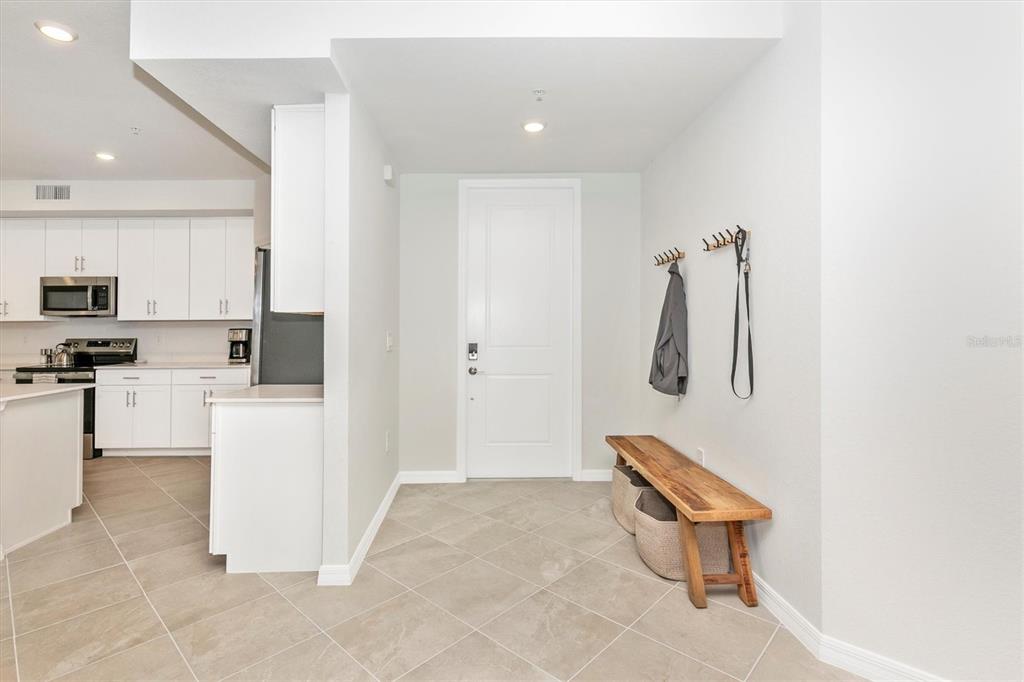 An entryway with tile flooring, a wooden bench, and a coat rack leads to a kitchen — 12685 RADIANCE COURT UNIT 102, VENICE, FL