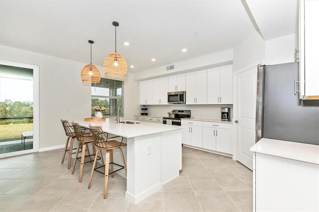 A bright kitchen features white cabinetry, a central island with bar stools, and tile flooring — 12685 RADIANCE COURT UNIT 102, VENICE, FL