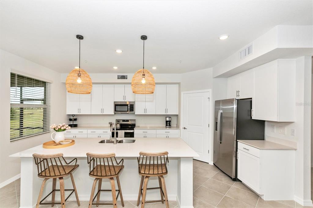 A modern kitchen features white cabinetry, a large island with three stools, and stainless appliances — 12685 RADIANCE COURT UNIT 102, VENICE, FL