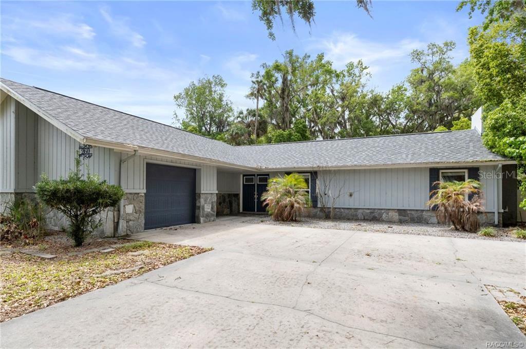 A single-story house with light gray vertical siding, a stone base, and a concrete driveway — 260 SE 16TH TERRACE, CRYSTAL RIVER, FL