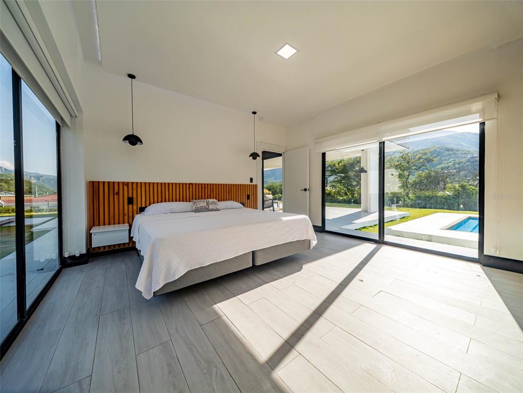 A modern bedroom features a wood-slat headboard, light tile floors, and large sliding glass doors — 00 CEIBOPAMBA BARRIO EL ALGODONAL, LOJA/ ECUADOR, NY