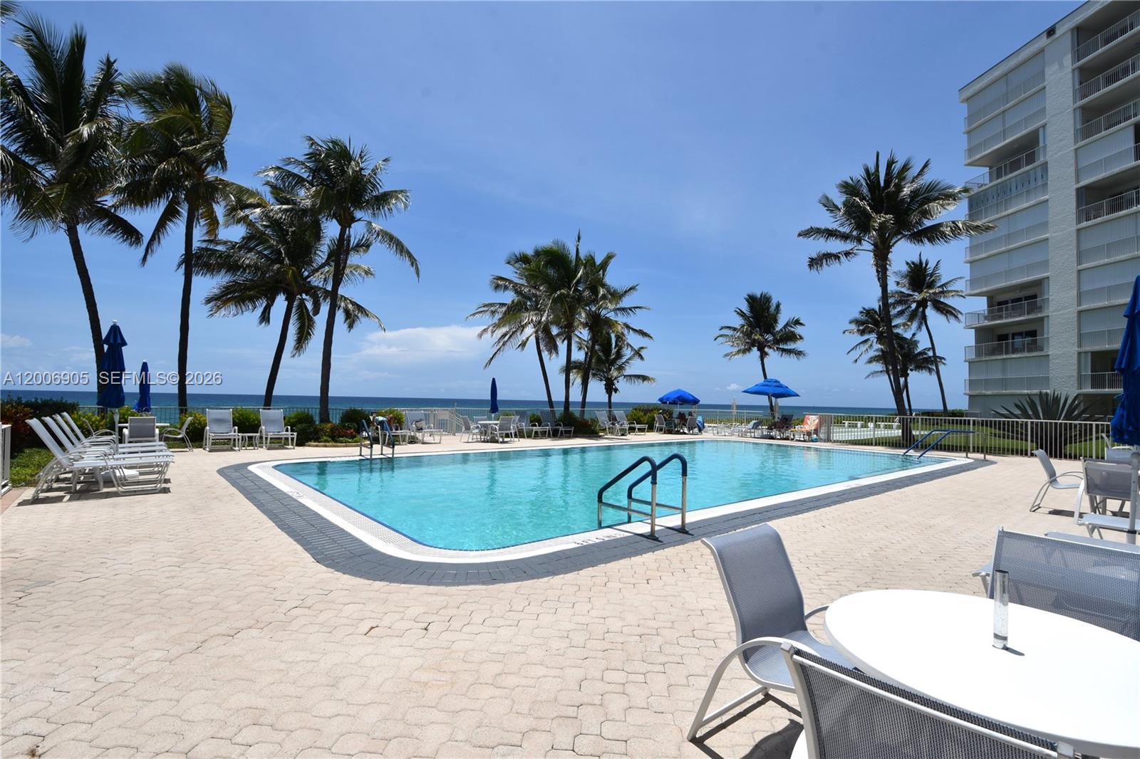A rectangular swimming pool is surrounded by a paved deck, palm trees, and lounge chairs — 3101 S Ocean Blvd # 118, Highland Beach FL 33487, HIGHLAND BEACH, FL