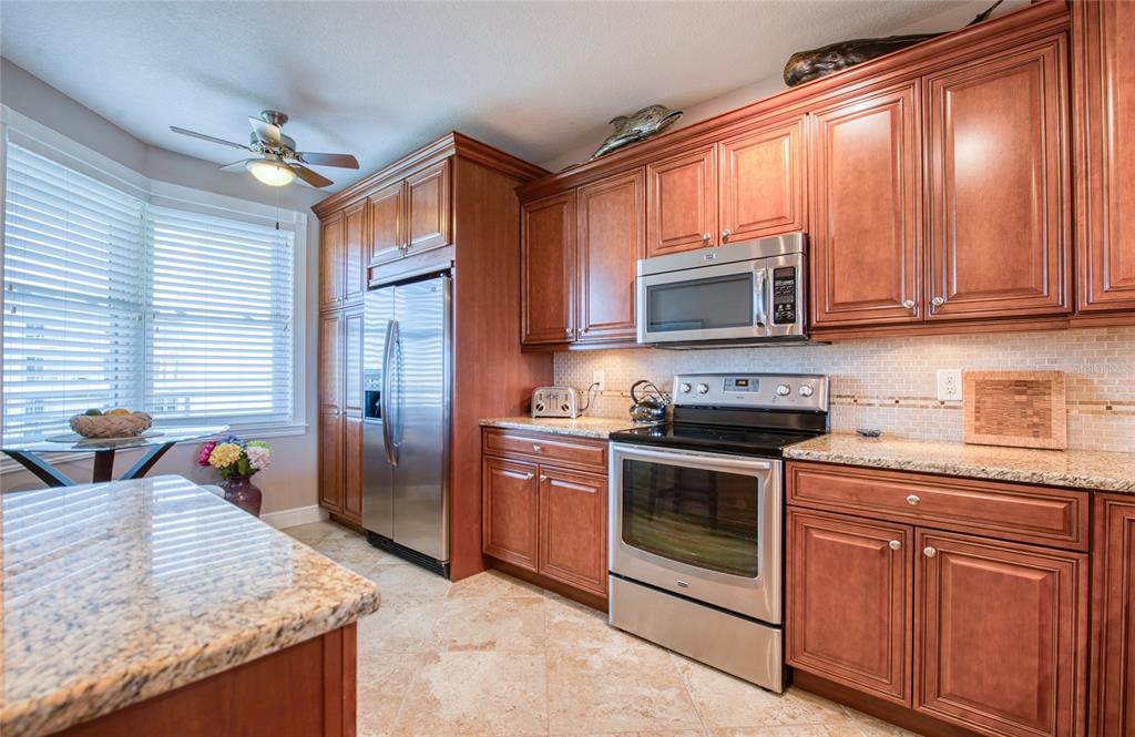 A kitchen features wood cabinets, stainless steel appliances, granite countertops, and tile flooring — 7984 SAILBOAT KEY BOULEVARD S UNIT 502, SOUTH PASADENA, FL