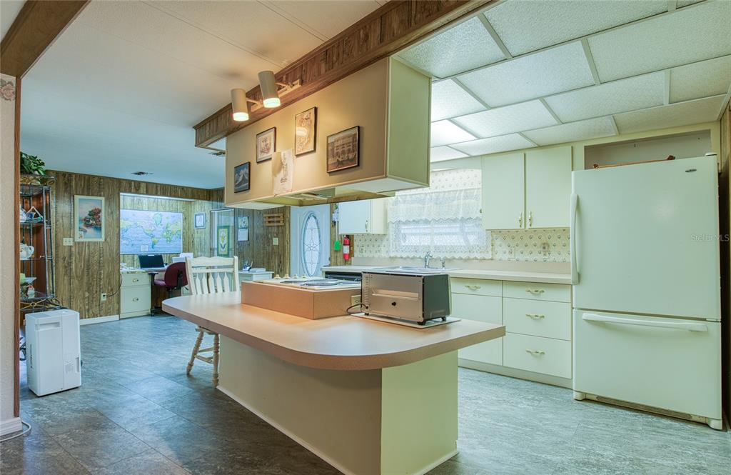 A kitchen features a central island, light-colored cabinetry, and wood-paneled walls in the adjacent room — 86 COTTAGEWOOD DRIVE UNIT 36, SAFETY HARBOR, FL