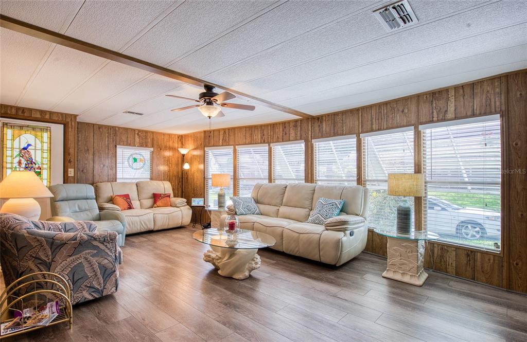 A living room features wood-paneled walls, light-colored sofas, a glass coffee table, and wood flooring — 86 COTTAGEWOOD DRIVE UNIT 36, SAFETY HARBOR, FL