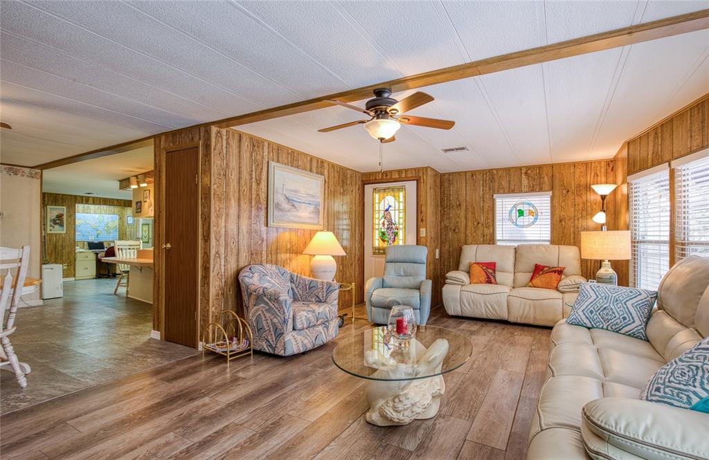 A living room features wood-paneled walls, wood-look flooring, a ceiling fan, and cream-colored furniture — 86 COTTAGEWOOD DRIVE UNIT 36, SAFETY HARBOR, FL
