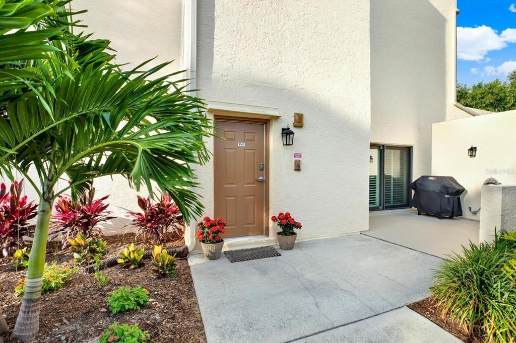 A tan stucco building exterior features a brown front door, potted flowers, and a patio — 7530 SUNSHINE SKYWAY LANE S UNIT P7, ST PETERSBURG, FL
