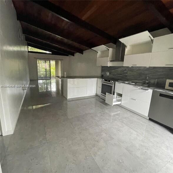 A modern kitchen features white cabinets, stainless steel appliances, and a dark wood beamed ceiling — 112 Fox Rd # 50, Hollywood FL 33024, HOLLYWOOD, FL