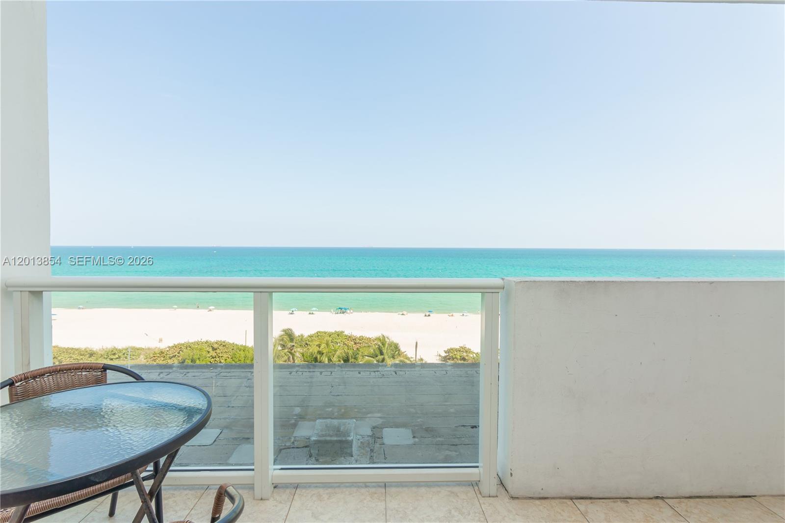 A balcony with a glass railing overlooks a sandy beach and the ocean — 5445 Collins Ave # 627, Miami Beach FL 33140, MIAMI BEACH, FL