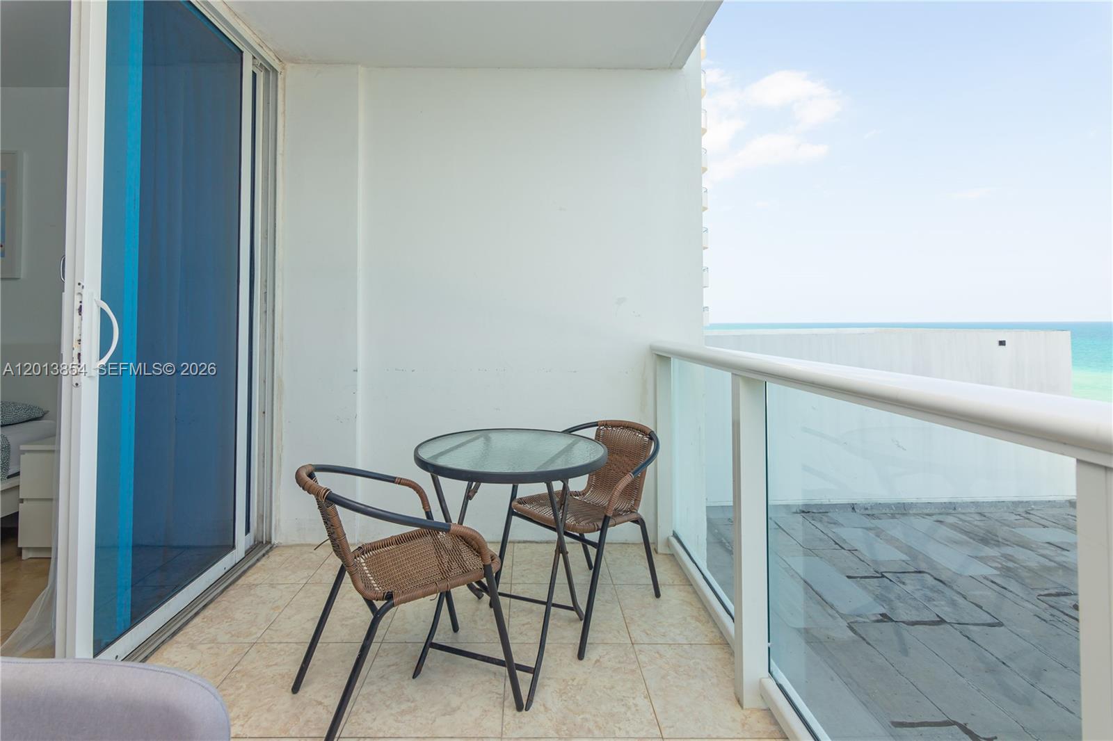 A balcony features a small glass-top table and two chairs overlooking the ocean — 5445 Collins Ave # 627, Miami Beach FL 33140, MIAMI BEACH, FL
