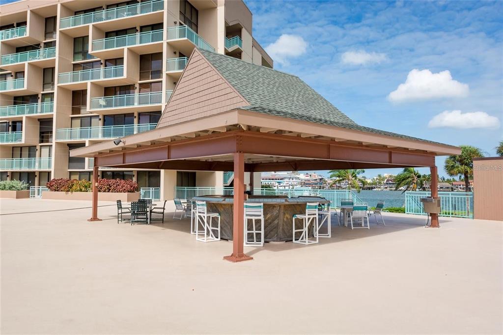 An outdoor covered bar area with seating sits on a patio beside a large building — 1 KEY CAPRI UNIT 302E, TREASURE ISLAND, FL