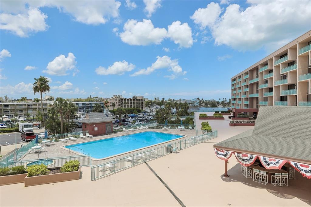 An elevated view of a swimming pool, patio area, and multi-story building under a blue sky — 1 KEY CAPRI UNIT 302E, TREASURE ISLAND, FL