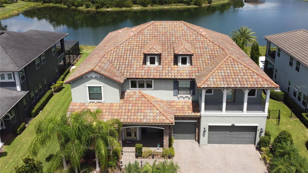 An aerial view of a two-story house with a tiled roof and a lake behind — 18014 WOODLAND VIEW DRIVE, LUTZ, FL